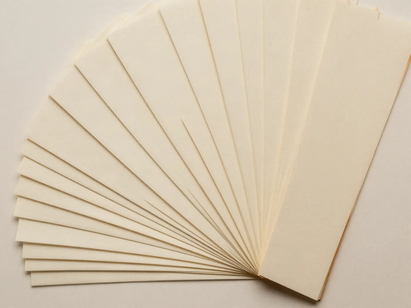 A fan of plain paper sheets spread across a warm neutral surface.